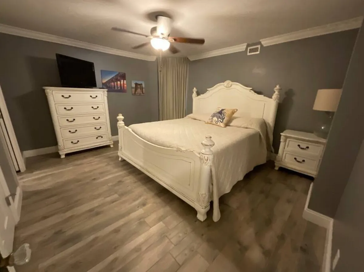 A restful bedroom with a comfortable bed, dresser, nightstand, ceiling fan, and elegant wall art. The atmosphere exudes serenity, highlighted by soft lighting and thoughtful décor—ideal for relaxation and peaceful sleep.