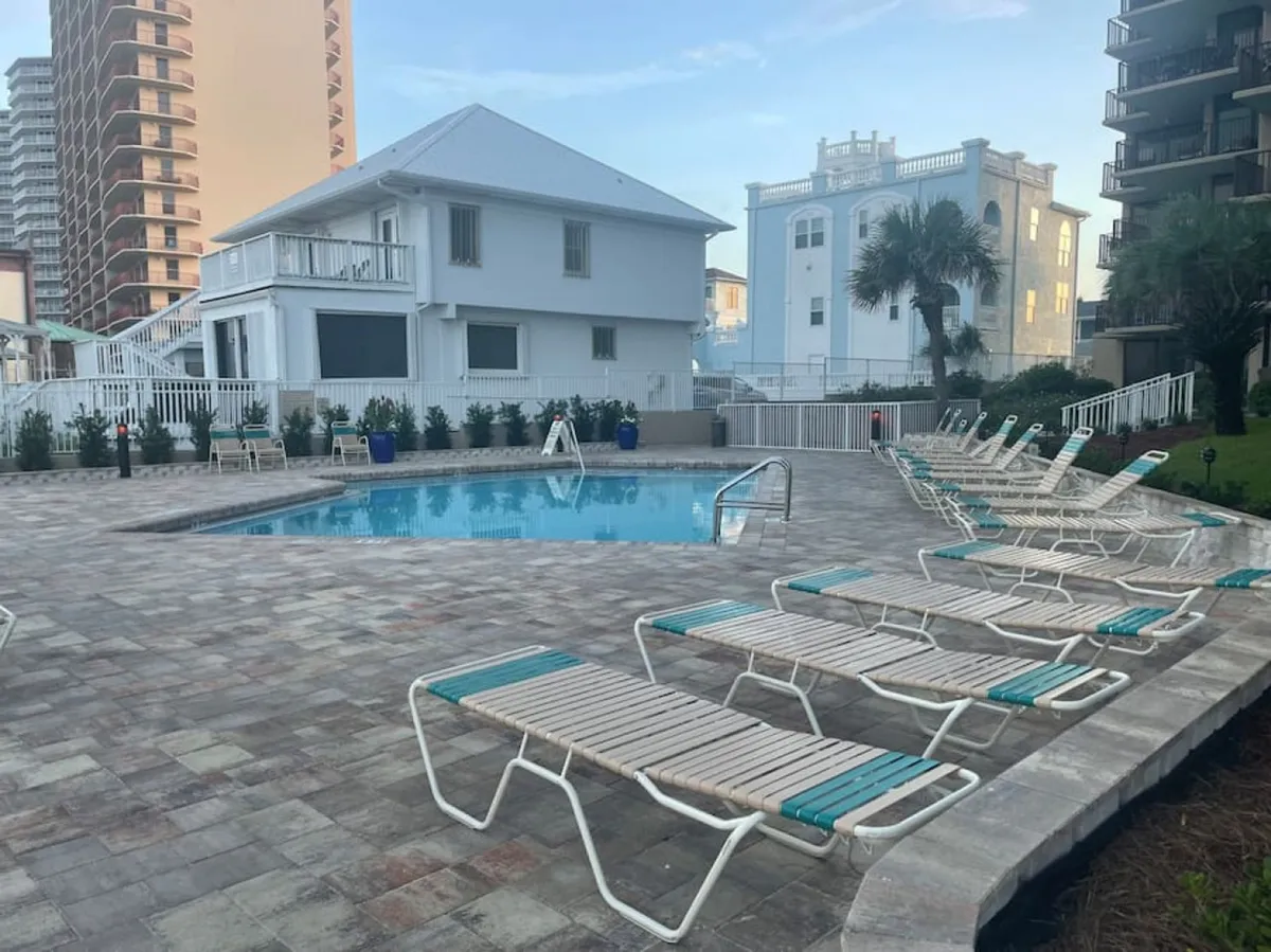 An inviting exterior showing a swimming pool surrounded by lounge chairs and nearby buildings. The environment suggests a convenient, social atmosphere where residents can unwind, swim, or enjoy time with family and friends, all in close proximity to the condo.