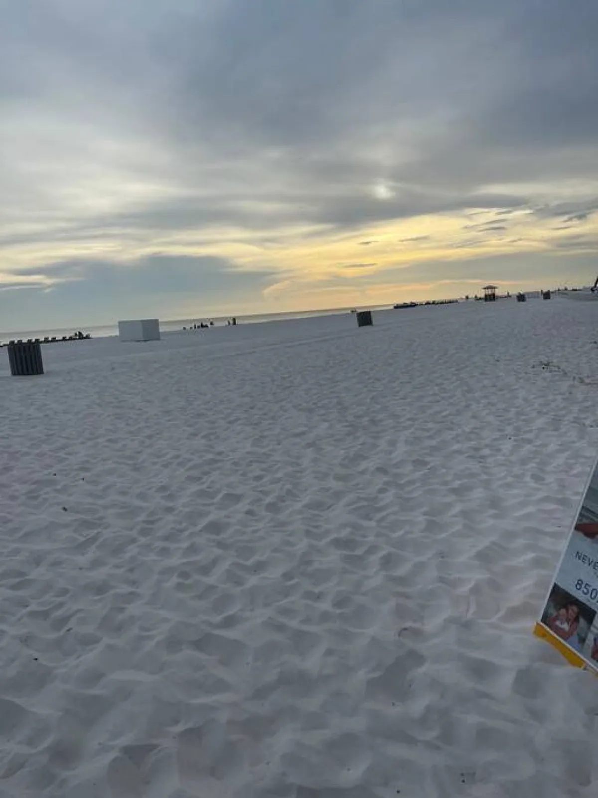A tranquil beach scene with the ocean, sky, and distant figures walking or socializing. The wide angle captures the open, accessible shoreline that residents can stroll to, reinforcing the idea that local attractions (like the beach and nearby dining) are within easy reach and part of daily life.