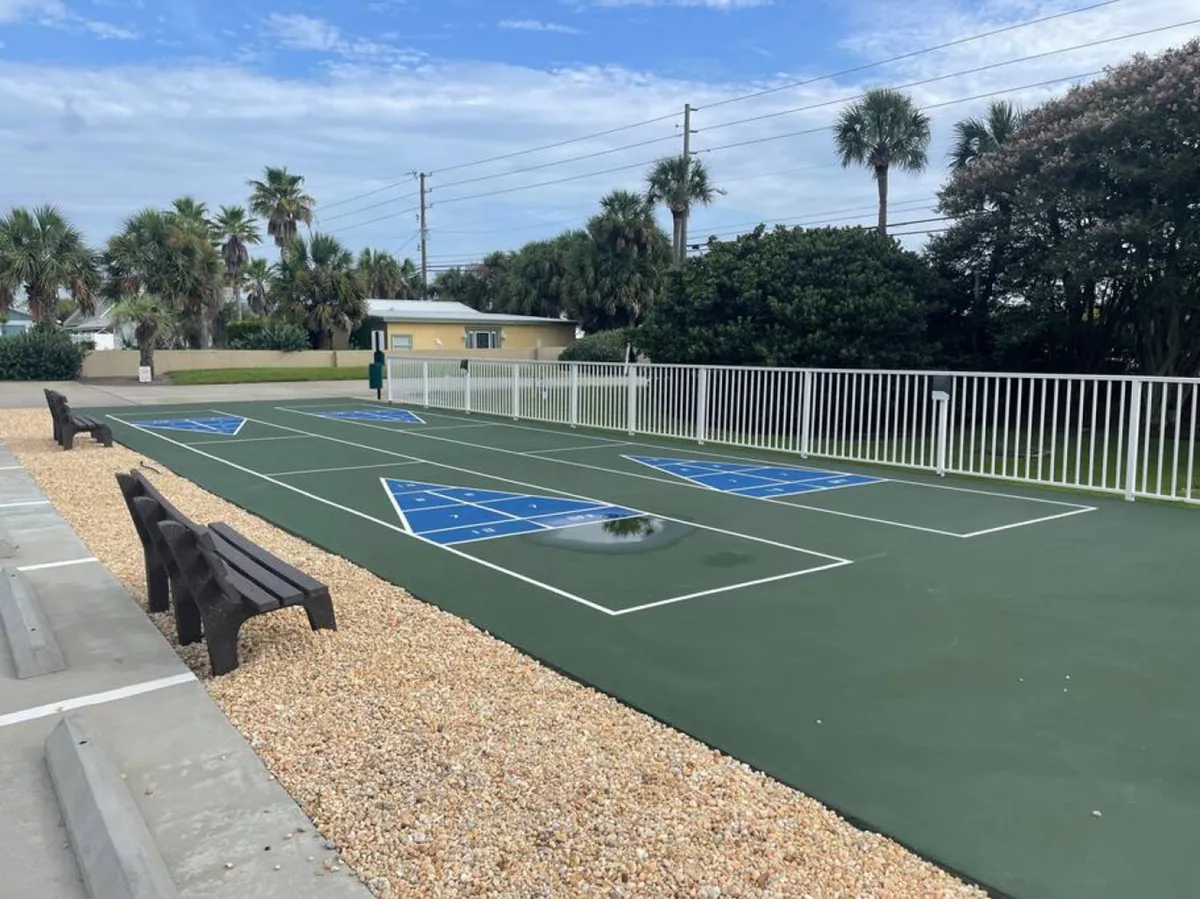 This playful exterior shot features shuffleboard courts, benches, and people socializing under palm trees. The setting is relaxed and communal, capturing leisure and the opportunity for casual fun just outside the condo, which matches the theme of local adventures and gathering with friends.
