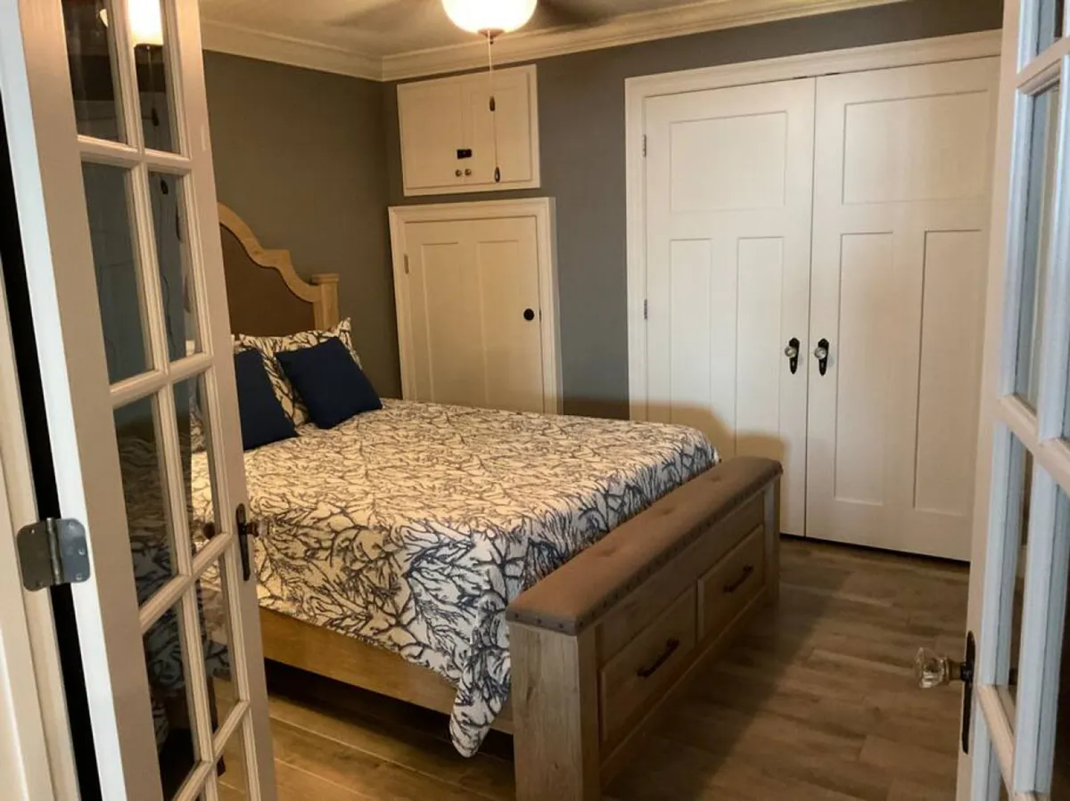A guest bedroom with a wooden bed frame, patterned bedding, blue accent pillows, double white closet doors, and a wooden bench at the foot of the bed. The room feels cozy, inviting, and ideal for restful sleep or quiet moments.