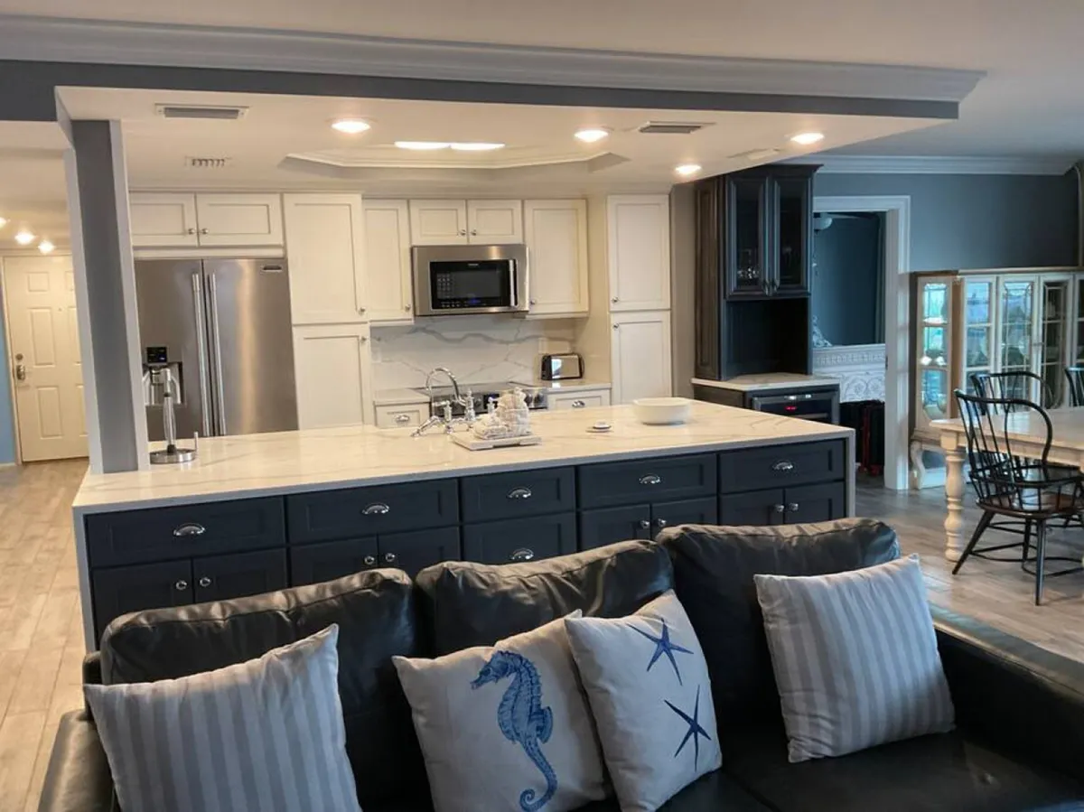 A welcoming kitchen and dining space with a large island featuring a marble countertop, a stainless steel refrigerator, and a cozy dining area with black chairs. Decorative sea-themed pillows and a soft couch add a touch of homey comfort, reinforcing the family-friendly vibe.